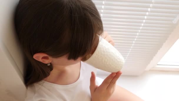 Hermosa chica se sienta en el alféizar de la ventana cerca de ventana y bebe té con limón . — Vídeos de Stock