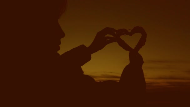 Ensam siluett av en tjej med ett hjärta på en vacker solnedgång och ljusa solen. — Stockvideo