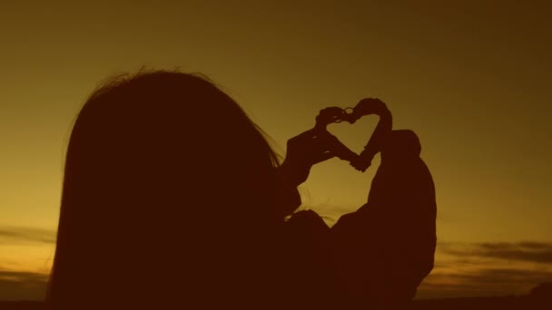 Osamělý silueta dívky drží srdce na krásný západ slunce a jasné slunce. — Stock video