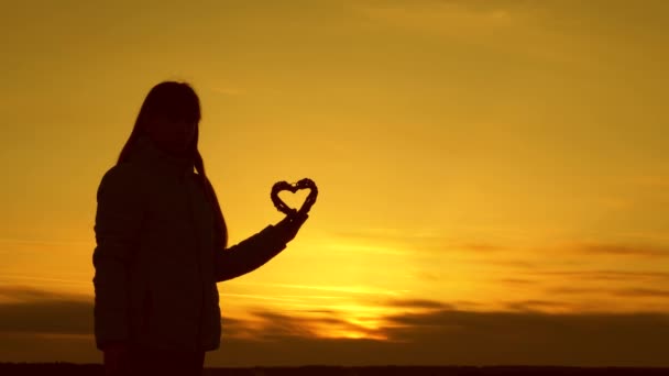 Ensom silhuet af en pige, der holder et hjerte på en smuk solnedgang og den lyse sol . – Stock-video