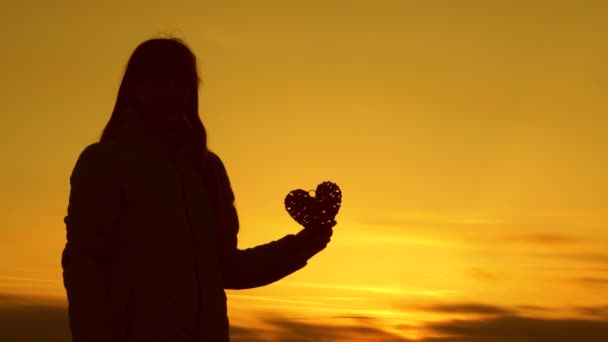 Osamělý silueta dívky drží srdce na krásný západ slunce a jasné slunce. — Stock video