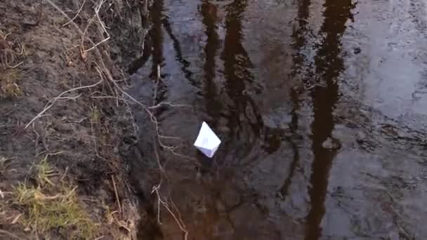 Bateau en papier blanc navigue le long de la rive de la rivière et il est poussé avec un bâton . — Video