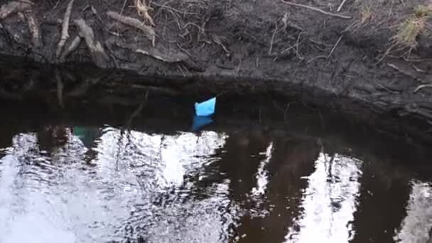 Голубая бумажная лодка из цветной бумаги плавает вдоль берега реки . — стоковое видео
