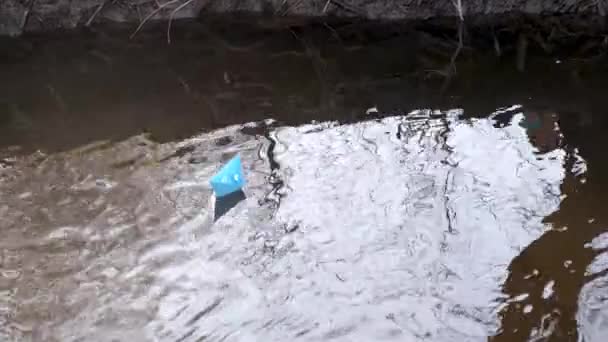 Blått papper båt av färgat papper flyter längs flodstranden. — Stockvideo