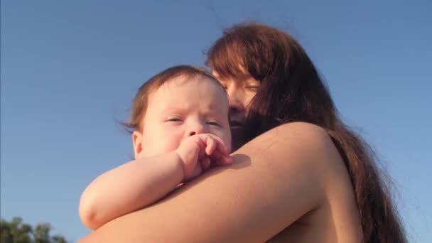 母親と小さな赤ちゃんが青い空を背景に抱擁します。. — ストック動画