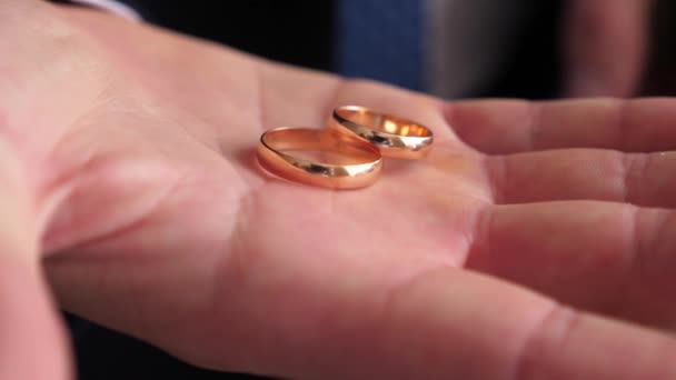 Novio sosteniendo anillos de boda de oro en su mano — Vídeo de stock