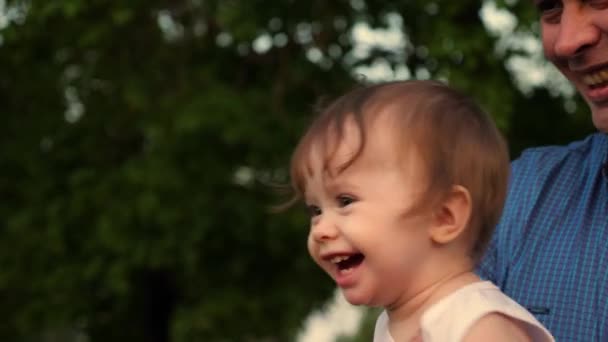 Le bébé rit des mains de son père aimant. Bébé et papa rient, jouant ensemble pour une promenade dans le parc . — Video