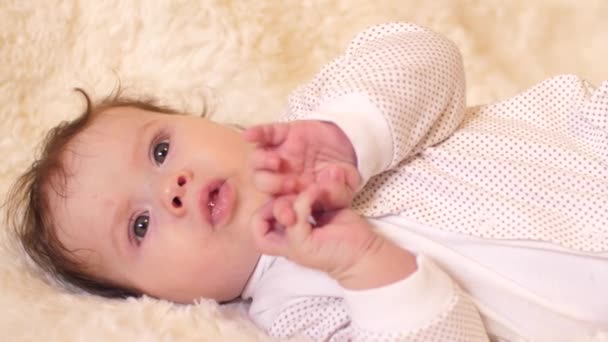 Baby ligt op zijn rug en speelt met zijn handen. Slow motion. — Stockvideo