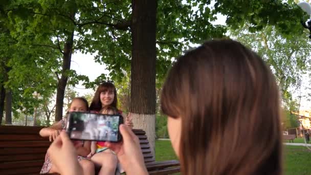 Chica joven toma fotos de su madre, hermana y niño pequeño en el teléfono . — Vídeos de Stock