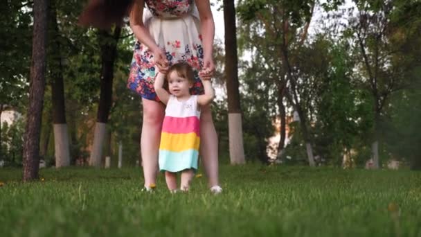 Mom teaches her little daughter to walk with her feet, holding her hands. — Stock Video
