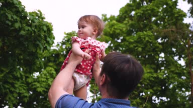 Genç Baba ve bebek birlikte dışarıda oynarken gülüyor. Kız havada üst ve gülümseyen boyuyla atlıyor. Ağır çekim.