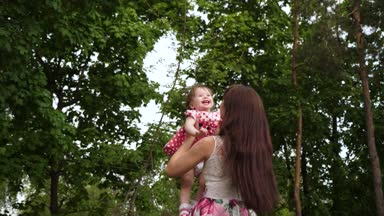 O havada uçtuğu zaman kız anne kucağında güler. Anne kucağında neşeli bebek tutan ve yeşil parkta yürüyor. Anne tarafından mutluluk. Ağır çekim.