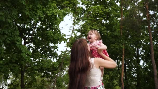 La ragazza ride tra le braccia della madre quando vola in aria. Mamma tiene in braccio un bambino allegro e cammina nel parco verde. Felicità materna. Rallentatore . — Video Stock