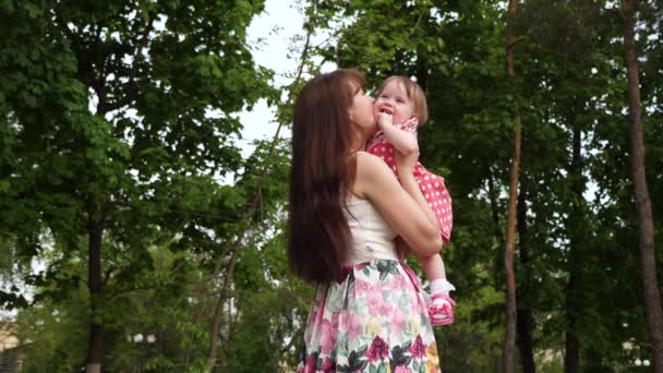 Maminka má dítě v náručí a políbí na tvář. Holka se směje se svými rodiči v zeleném parku. Zpomalený pohyb. — Stock video