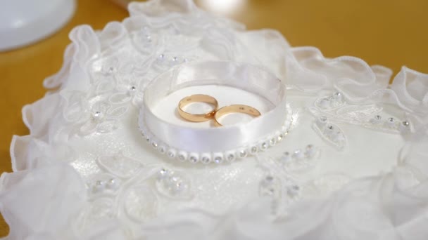 Anillos de boda de oro se encuentran en una caja blanca en una hermosa almohada con encaje y diamantes de imitación — Vídeo de stock