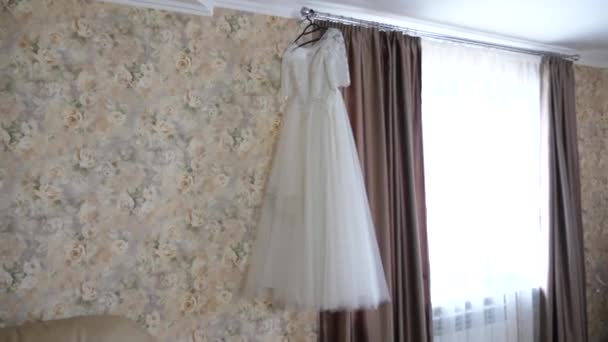 Красивое белое свадебное платье висит на вешалке у окна — стоковое видео