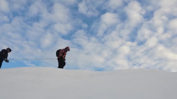 Squadra di scalatori legati con una corda di sicurezza cammina in inverno lungo la cima di una montagna innevata. I viaggiatori si susseguono lungo una cresta innevata. turismo di squadra ben coordinato in inverno — Video Stock