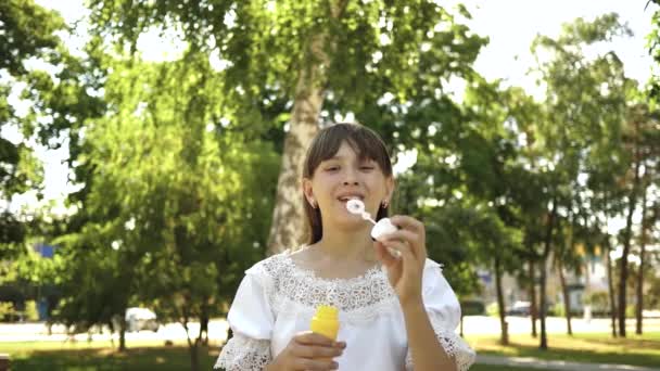 Šťastná dívka foukání krásné mýdlové bubliny v parku na jaře, v létě a s úsměvem. Zpomalený pohyb. mladá dívka projíždějící městem v parku. — Stock video