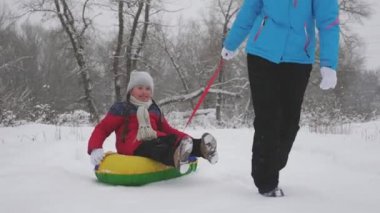 Çocuk ve anne karda kayıyorlar. Kız ve anne Noel tatillerinde kış parkında oynuyorlar. Aile kış tatili. Mutlu çocukluk kavramı
