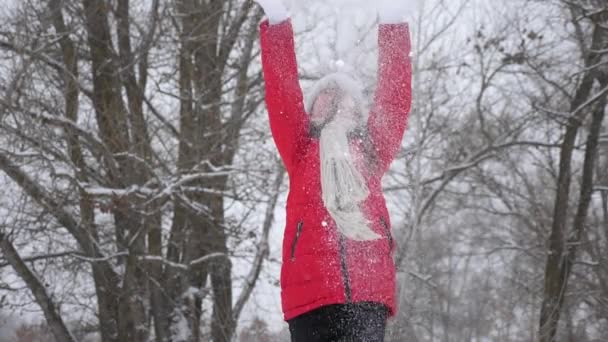 Niña feliz lanza nieve con las manos en el bosque. Nieve cae y brilla al sol. niño juega en invierno en el parque para las vacaciones de Navidad . — Vídeos de Stock