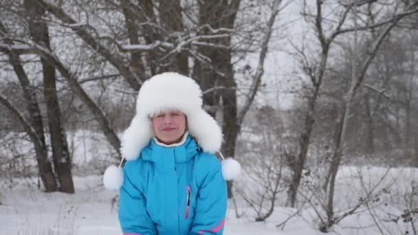 Chica feliz lanza nieve con las manos en el bosque y se ríe. La nieve cae y brilla al sol. Una mujer juega en el invierno en el parque para las vacaciones de Navidad — Vídeos de Stock