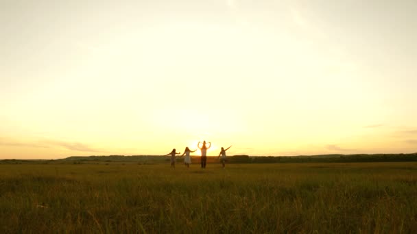 Feliz familia joven con un niño corriendo a través del campo en la luz del atardecer. madre, padre e hija pequeña con hermanas caminando en el parque. Niños, papá y mamá juegan en el prado bajo el sol . — Vídeos de Stock