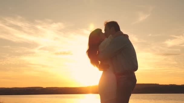 Happy man and girl kiss and cuddle at sunset on the beach. Loving man and woman in a romantic setting in the sun on a lake. The concept of family relationships. Slow motion — Stock Video