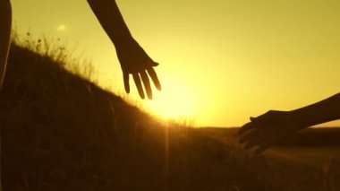 Gezginler, gün batımında el ele tutuşarak ve birbirini çekerek yüksek bir dağın zirvesini fethetmede birbirlerine yardım ederler. Yürüyüşçü kız. Aile turizmi. Cesaret için zorlu bir yürüyüş. Takım çalışması gezginleri.