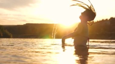 neşeli kız ferahlatıcı bir nehir suyu ile tropikal adanın yakınında ferahlatıcı bir yaz akşamı onu uzun saçları sıçraması. Kız geri saç çevirir. gün batımı ışınları su güzel sprey. su sıçrama