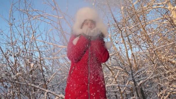 夕暮れ時に雪の結晶を吹いて、冬の公園で笑顔の幸せな女の子。スローモーション。冬の森の中で雪片を手から吹いてる子供はクリスマス休暇のために公園で冬に遊ぶ. — ストック動画