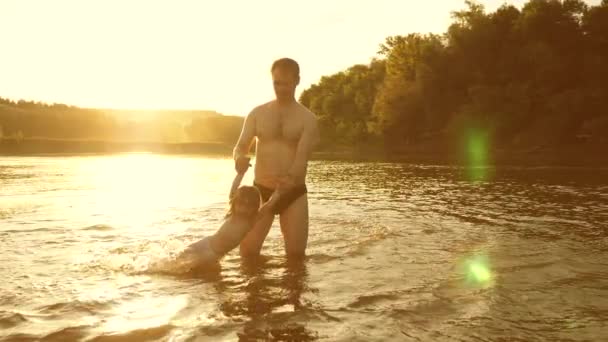 Otec a dcerka hrají ve vodě na pláži v teplém slunci. Šťastný otec a radostný úsměv, vykoupat a hrát ve vodě ve zlatém slunci. — Stock video