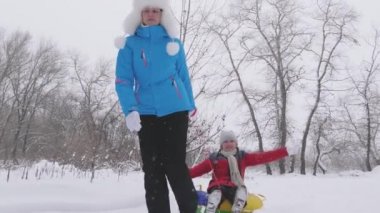 Çocuk ve anne karda kayıyorlar. Kız ve anne Noel tatillerinde kış parkında oynuyorlar. Aile kış tatili. Mutlu çocukluk kavramı