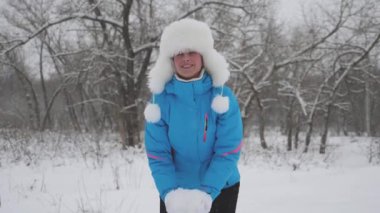 Mutlu kız ormanda elleri havada kar atıyor ve gülüyor. Kar yağar ve güneşte parlar. Bir kadın Noel tatili için parkta oynuyor.