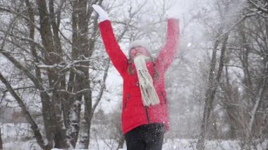 Mutlu kız çocuğu elleriyle ormana kar fırlatıyor. Kar yağar ve güneşte parlar. Çocuk Noel tatili için parkta oynuyor.