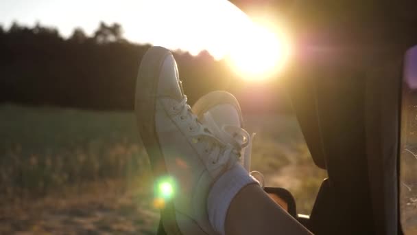 Pernas de uma menina em uma janela de carro, brilho do sol, montando um carro em uma estrada rural. uma jovem gosta de viajar em um carro, colocando suas pernas fora de uma janela aberta . — Vídeo de Stock