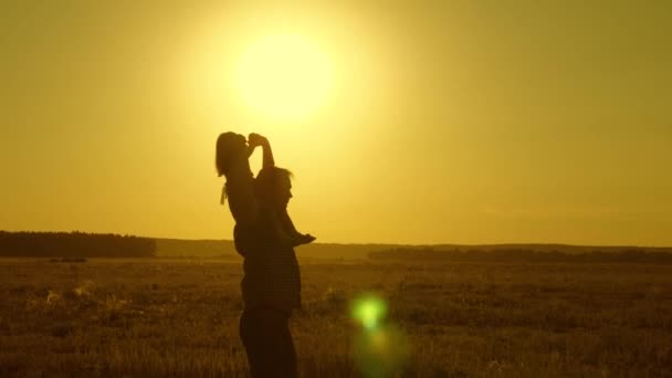 Papa porte bébé bien-aimé sur ses épaules marchant autour du champ au coucher du soleil. Un enfant avec ses parents se promène le soir au coucher du soleil. petite fille chevauchant avec papa sur ses épaules dans le parc. Mouvement lent . — Video