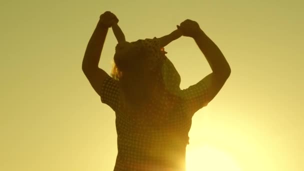 Papá lleva al amado bebé sobre sus hombros caminando alrededor del campo al atardecer. hija pequeña montando con papá sobre sus hombros en el parque. Un niño con sus padres camina por la noche al atardecer del sol. Movimiento lento . — Vídeo de stock