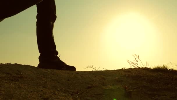 Een moedige man-reiziger, klimmen naar de top van een berg, wandelen langs een pad langs een gevaarlijke rotsachtige heuvelrug. Steile muur die een prachtig uitzicht op de zonsondergang opent. Slow Motion. Close-up. — Stockvideo