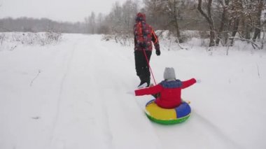 Mutlu baba, karlı bir yolda bir çocuğu kızaklıyor. Noel tatilleri. Baba, kızıyla kış parkında oynuyor. Mutlu aile kavramı. Bir genç Tubing 'e biniyor.