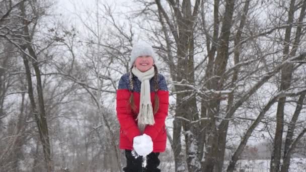Menina feliz joga neve com as mãos na floresta. A neve cai e brilha ao sol. criança joga no inverno no parque para férias de Natal . — Vídeo de Stock