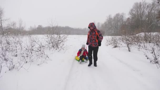 Mutlu baba, karlı bir yolda bir çocuğu kızaklıyor. Noel tatilleri. Baba, kızıyla kış parkında oynuyor. Mutlu aile kavramı. Bir genç Tubing 'e biniyor. — Stok video