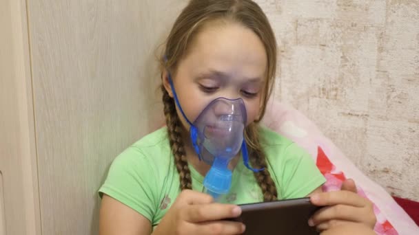 El niño con el comprimido está enfermo y respira a través de un inhalador. Primer plano. niña pequeña tratada con una máscara de inhalación en su cara en el hospital. El niño pequeño trata la gripe inhalando vapor de inhalación . — Vídeos de Stock