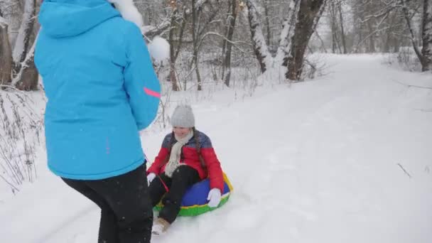Παιδί και μητέρα έλκηθρο στο χιόνι. Η κόρη και η μαμά παίζουν στο χειμερινό πάρκο τις γιορτές των Χριστουγέννων. οικογενειακές χειμερινές διακοπές. χαρούμενη έννοια παιδική ηλικία — Αρχείο Βίντεο