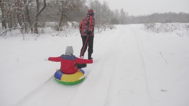 Mutlu baba, karlı bir yolda bir çocuğu kızaklıyor. Noel tatilleri. Baba, kızıyla kış parkında oynuyor. Mutlu aile kavramı. Gençler Tubing 'e biniyor — Stok video