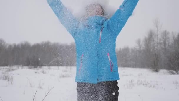 Szczęśliwa kobieta wymiotuje śniegiem rękami w lesie. Śnieg pada i błyszczy w słońcu. dziewczyna gra w zimie w parku na święta Bożego Narodzenia. — Wideo stockowe