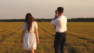 Mutlu baba kucağında küçük bir kız taşır ve sahada annesiyle oynar. Ebeveynler bir yürüyüş için çocukla oynarlar. Aile hayatı konsepti. Takım çalışması. Mutlu bir çocukluk kavramı