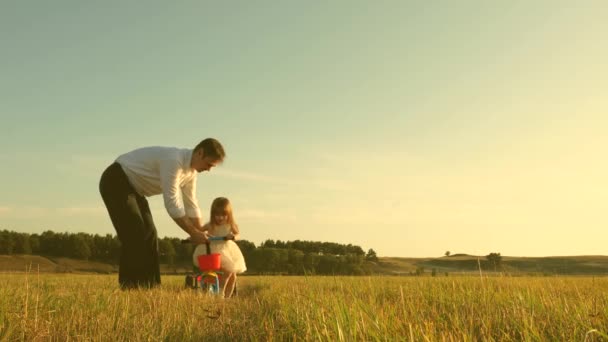 Szczęśliwy ojciec uczy córeczkę jeździć na rowerze. Tata bawi się z małym dzieckiem na trawniku. Dzieciak uczy się jeździć na rowerze. Rodzice i córeczka spacerują po parku. koncepcja szczęśliwej rodziny i dzieciństwa. — Wideo stockowe