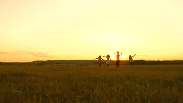 Szczęśliwa młoda rodzina z dzieckiem biegnie po polu o zachodzie słońca. Matka, ojciec i córki spacerują po parku i bawią się na łące w słońcu. Koncepcja życia dużej rodziny — Wideo stockowe