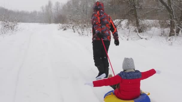 Heureux papa est chanceux sur un traîneau le long de la route blanche comme neige d'un enfant. Vacances de Noël et voyage. Un jeu amusant pour les adultes et les enfants. Le concept d'une famille heureuse. Un adolescent monte dans un tube — Video