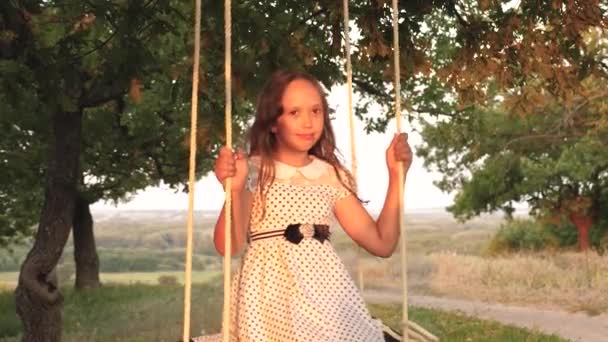 Happy childhood concept. child rides a rope swing on an oak branch in forest. girl laughs, rejoices. young girl swinging on a swing under a tree in sun, playing with children. Family fun in park. — Stock Video